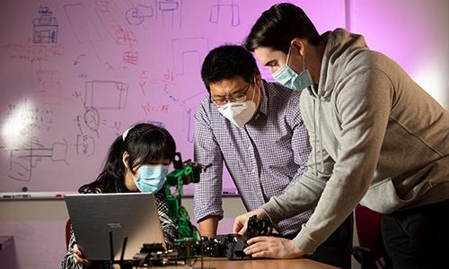 Two students with professor examining computer components